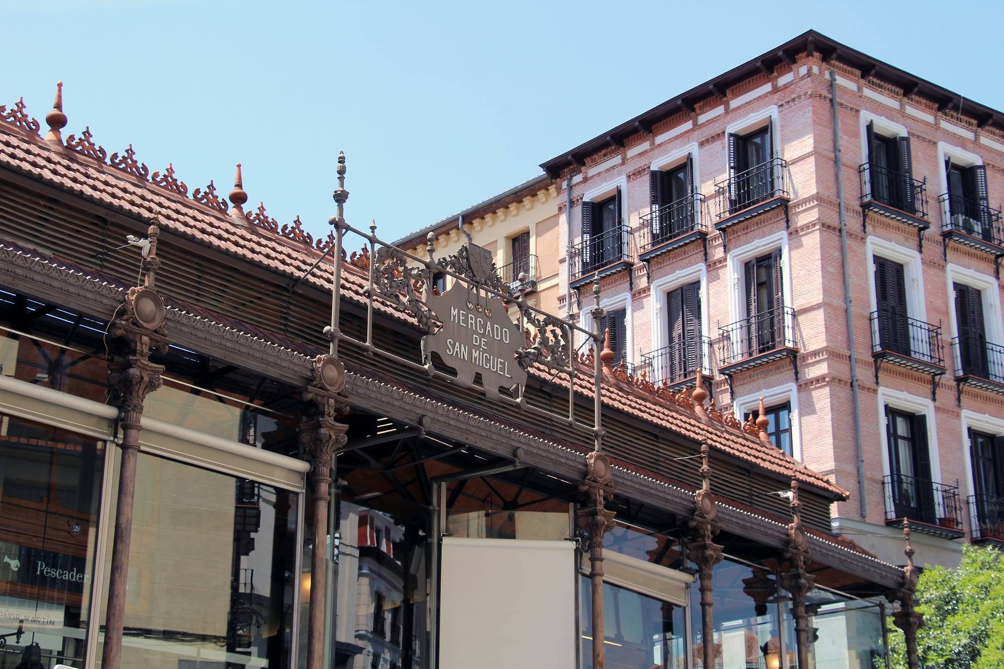 The cast-iron and glass Mercado de San Miguel next to the Plaza Mayor, with a pink residential building behind