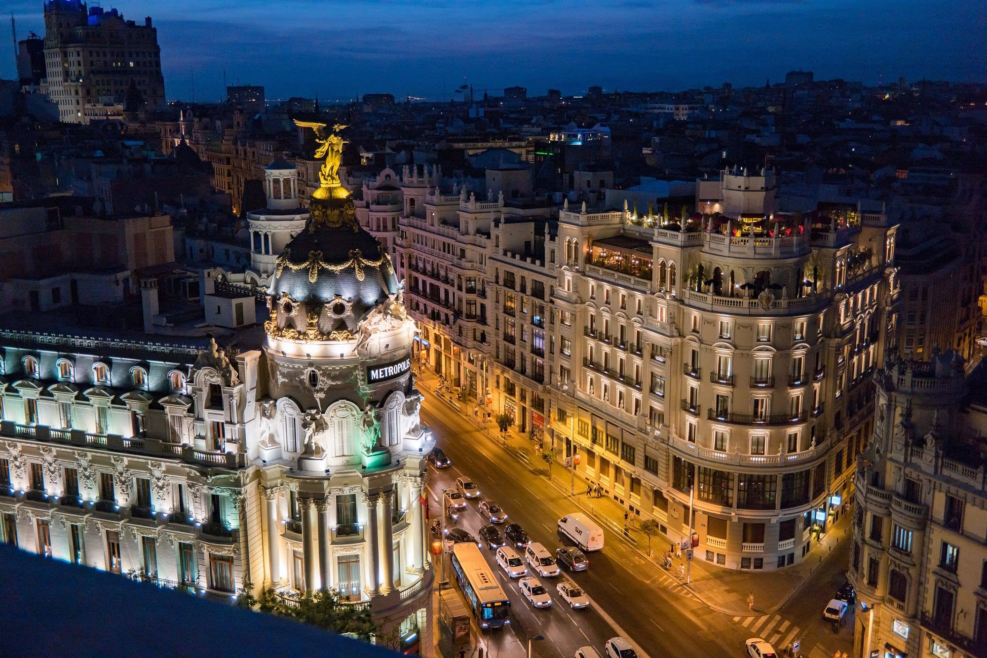 The domed Metrópolis building at the junction of Gran Vía and Calle de Alcalá, lit up at dusk above the traffic