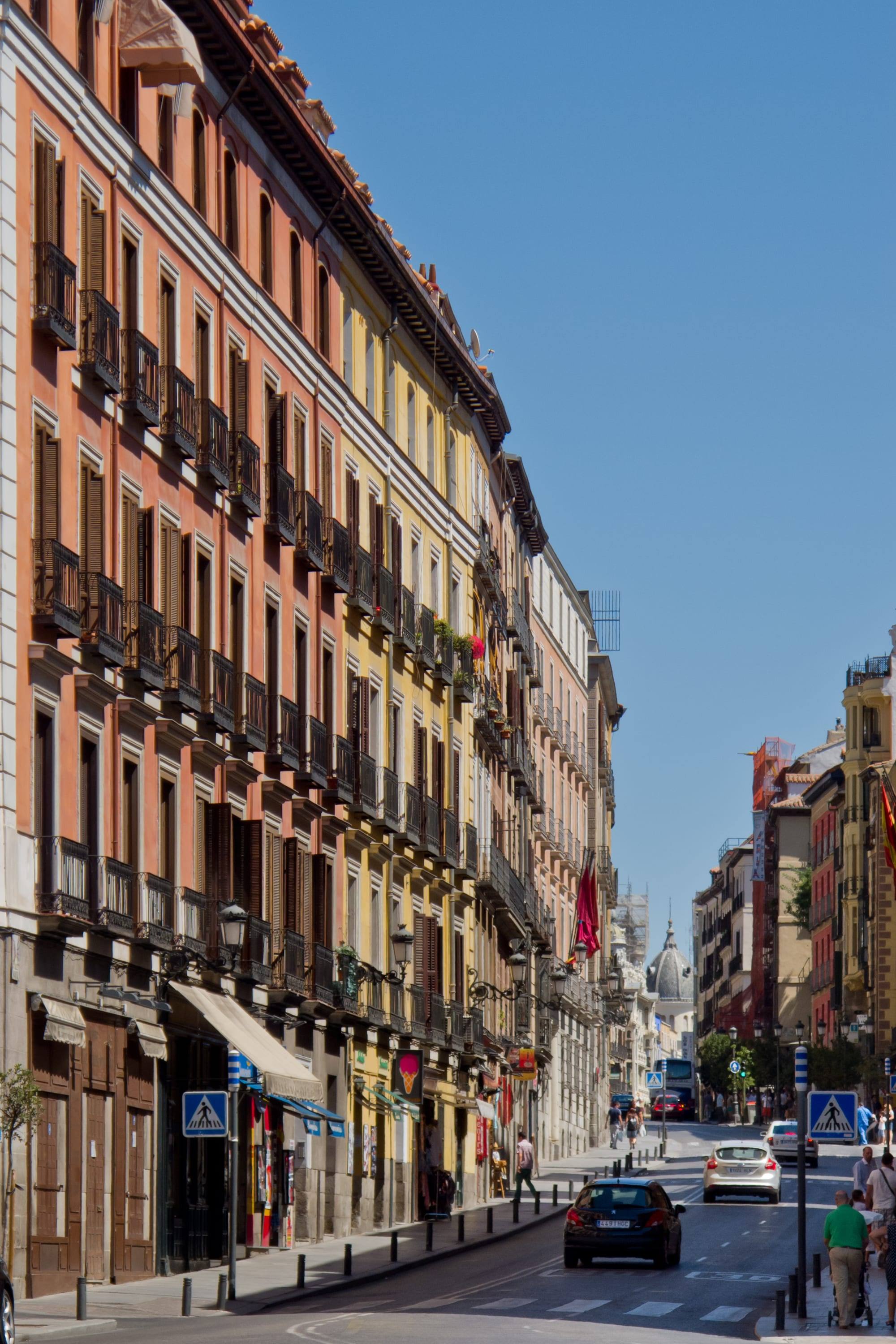 Calle Mayor in central Madrid, a straight street lined with tall 19th-century buildings with iron balconies, a church dome at its far end